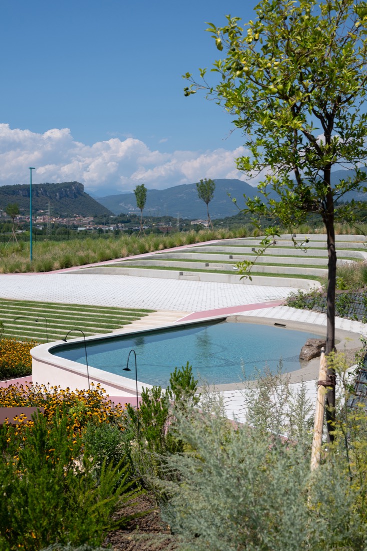 Piscina fra le aiuole, con i gradoni verdi e le montagne sullo sfondo
