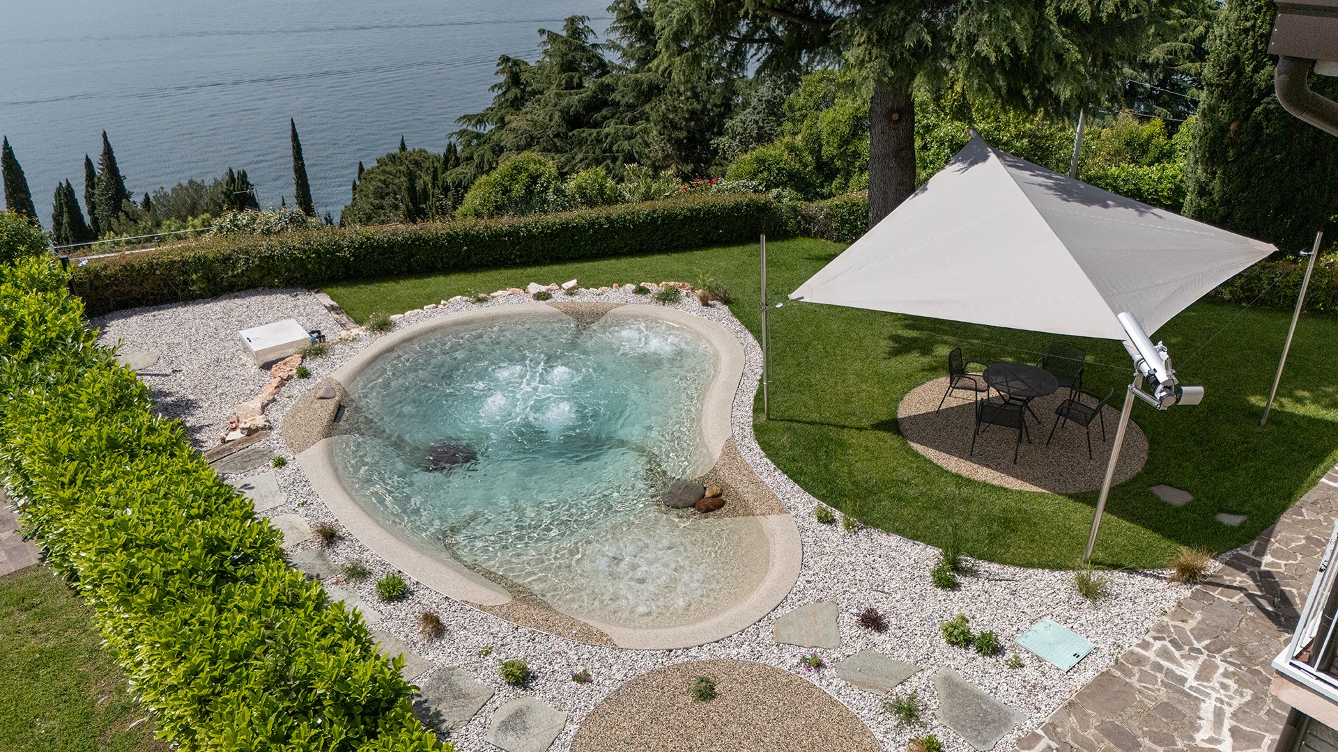 Piscina biodesign vista dall'alto, con la vela e il Lago di Garda sullo sfondo
